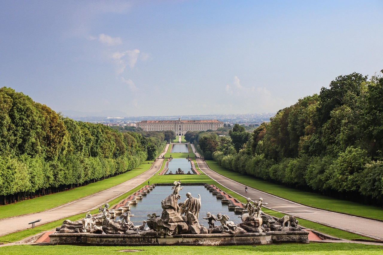 The Royal Palace of Caserta at the far end of the park's long central avenue of water, with a sculpted fountain in the foreground.