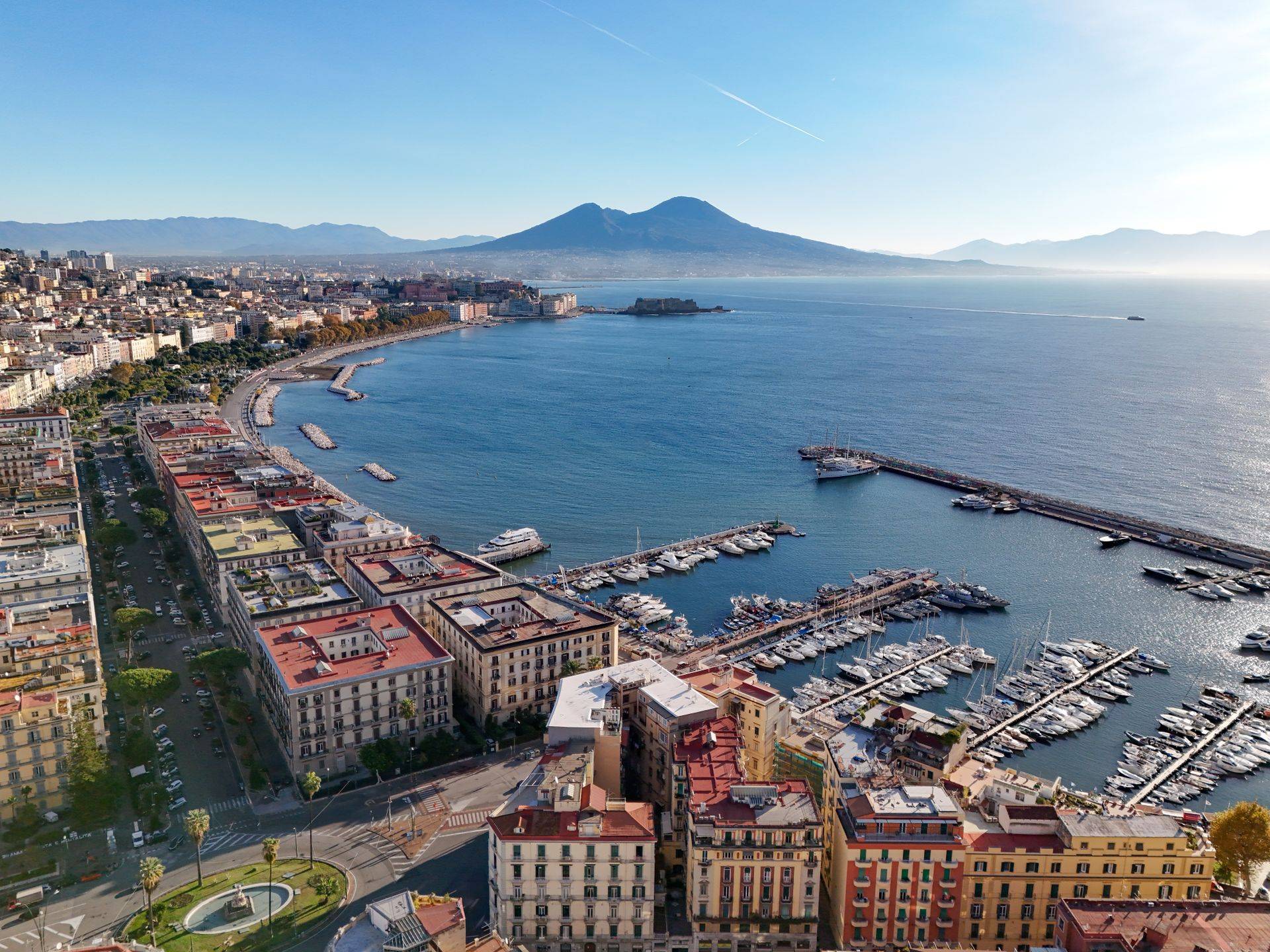 The Bay of Naples seen from above, with the seafront, a marina and Mount Vesuvius in the distance.